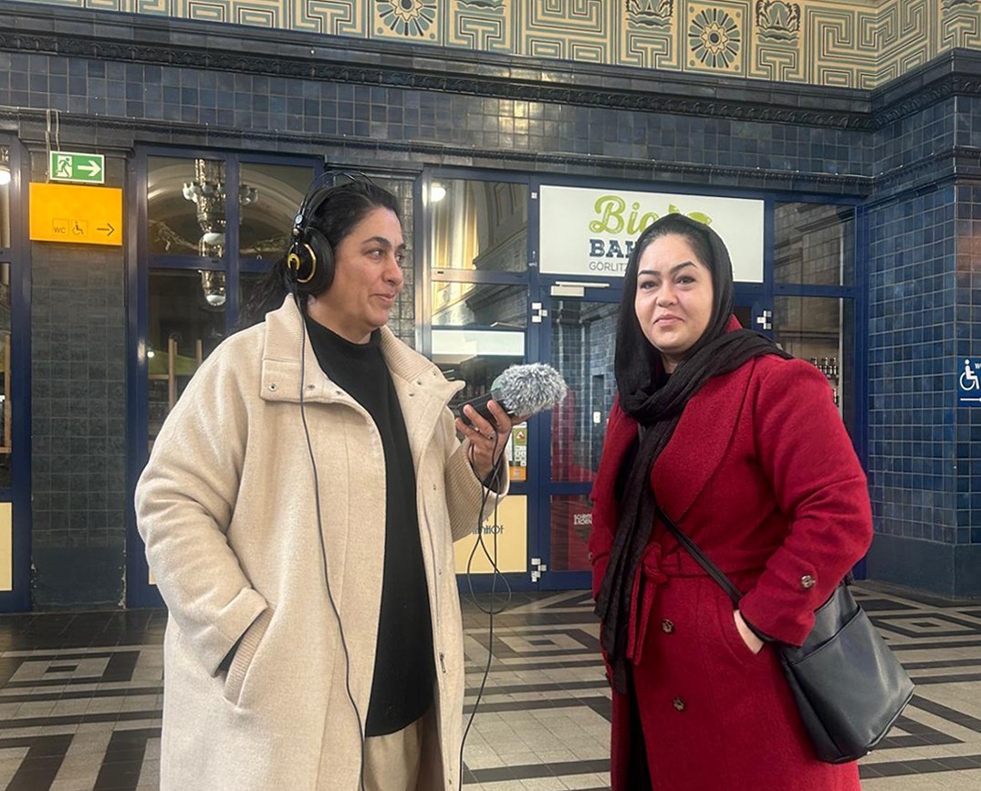 eine Afghanin mit Kopfhörer uns Aufnahmegerät interviewt eine andere Afghanin die die locker einen Schal um den Kopf geschwungen trägt.