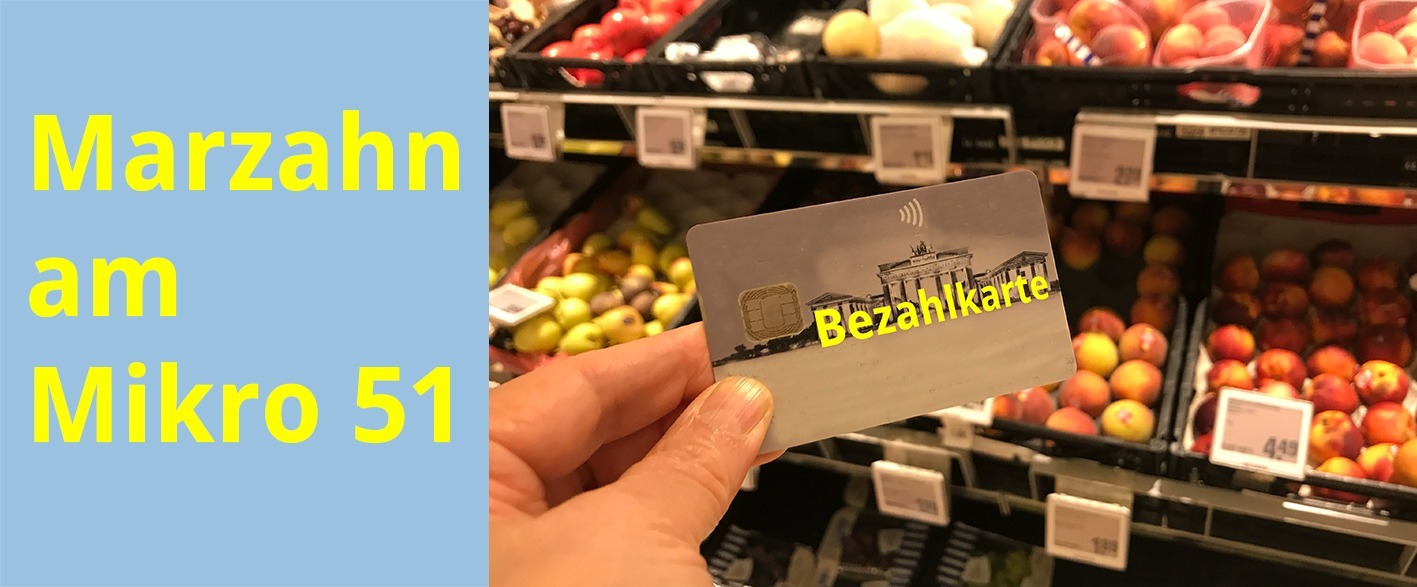 Eine Hand hält eine Bezahlkarte vor dem Obstregal in einem Supermarkt.