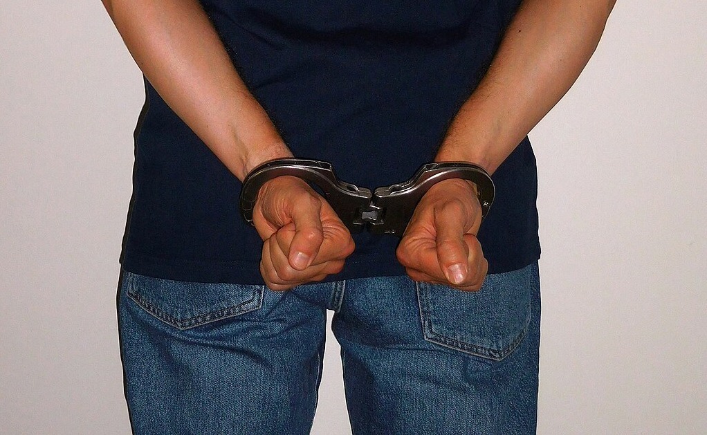 Ausschnitt: Mensch stehend Hände mit Handschellen hinter dem Rücken gefesselt