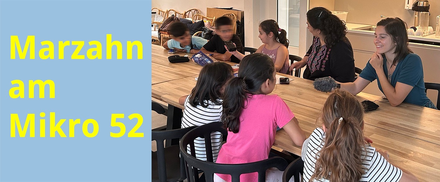 zusammen mit zwei Frauen sitzen 6 Kinder an einem Tisch und sprechen in Mikrofone.