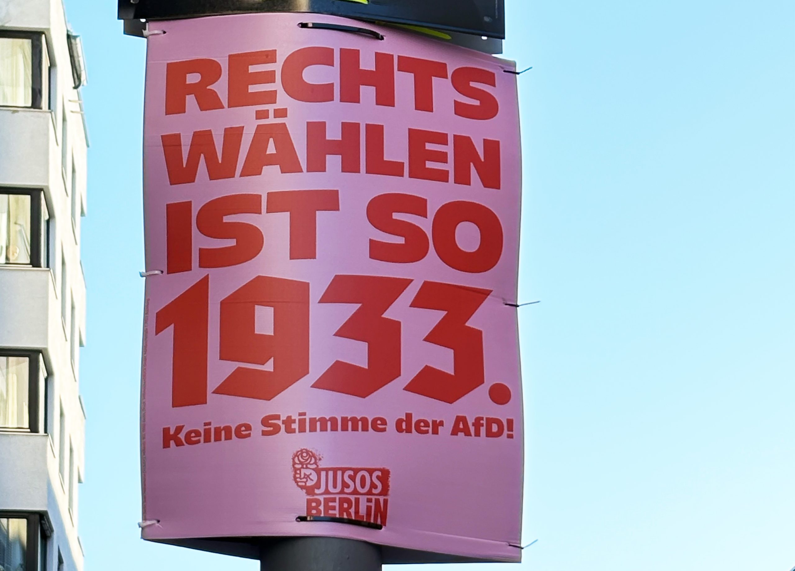 An einem Mast hängt ein eine Wahlwerbung der Jusos Berlin: Auf rosa Hintergrund steht in roter Schrift, Rechts wählen ist so 1933. Keine Stimme der AFD!